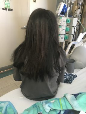 Hair and CF / Cystic Fibrosis News Today / Nicole sits on a hospital bed. Her hair is straight and down her back