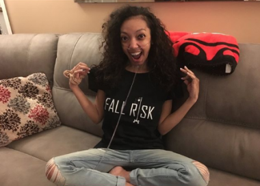 learn / Cystic Fibrosis News Today / Nicole sits on her couch wearing a black "Fall Risk" shirt and oxygen.