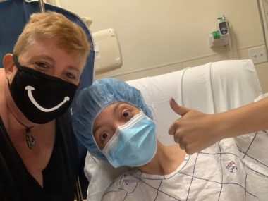 Cystic Fibrosis News Today \ Nicole and her mom pause for a photo ahead of Nicole's bronchoscopy in 2020. Nicole is wearing a hospital mask and scrubs, and her mom has a black mask with a smiley face.