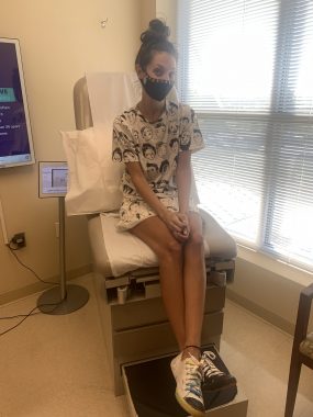 Cystic Fibrosis News Today | Bailey sits patiently in a chair in an examining room with a look of anticipation on her face, which is noticeable despite her facemask