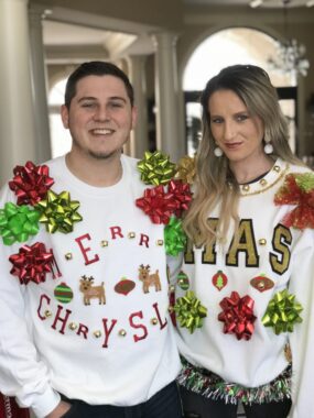 A brother and sister, both in their 20s, wearing matching white Christmas sweaters decorated with red and green bows.