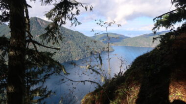 A postcard-like photo of a winding blue lake nestled in between majestic green mountains. 