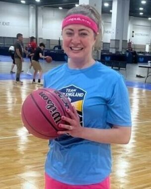 A woman holds a basketball as she stands on an empty basketball court.
