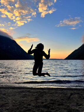 A woman is shown in silhouette at the beach, jumping into the air.